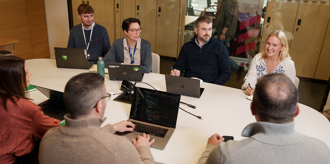 Business people sat talking around their laptops at a desk